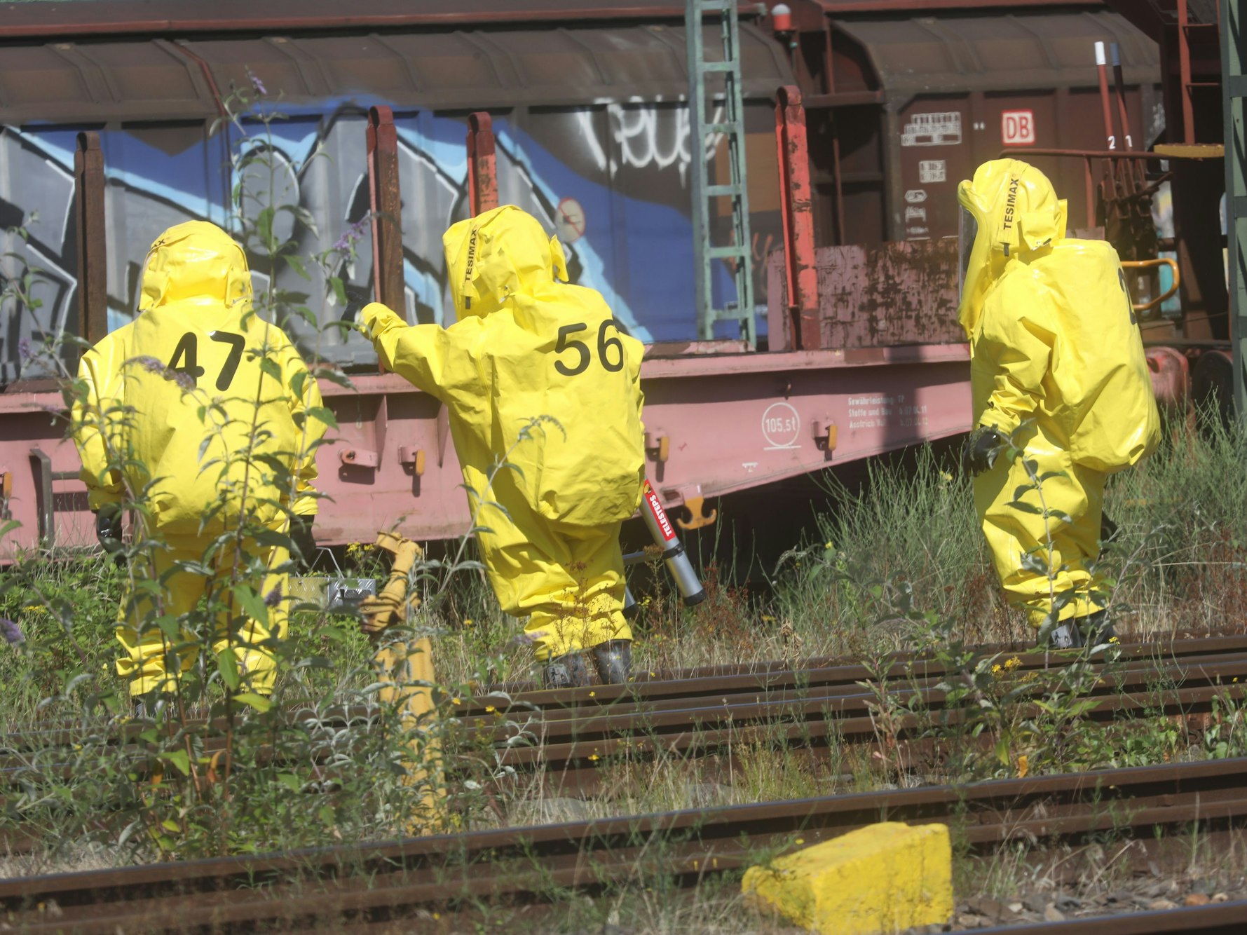 Feuerwehrleute stehen mit Schützanzügen an einem Güterwagon.