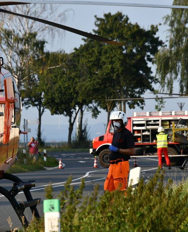 Einsatzkräfte stehen neben einem Rettungshubschrauber auf einer Landstraße.