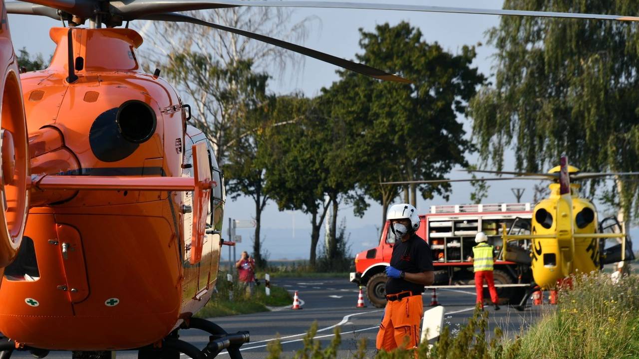 Einsatzkräfte stehen neben einem Rettungshubschrauber auf einer Landstraße.