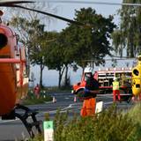 Einsatzkräfte stehen neben einem Rettungshubschrauber auf einer Landstraße.