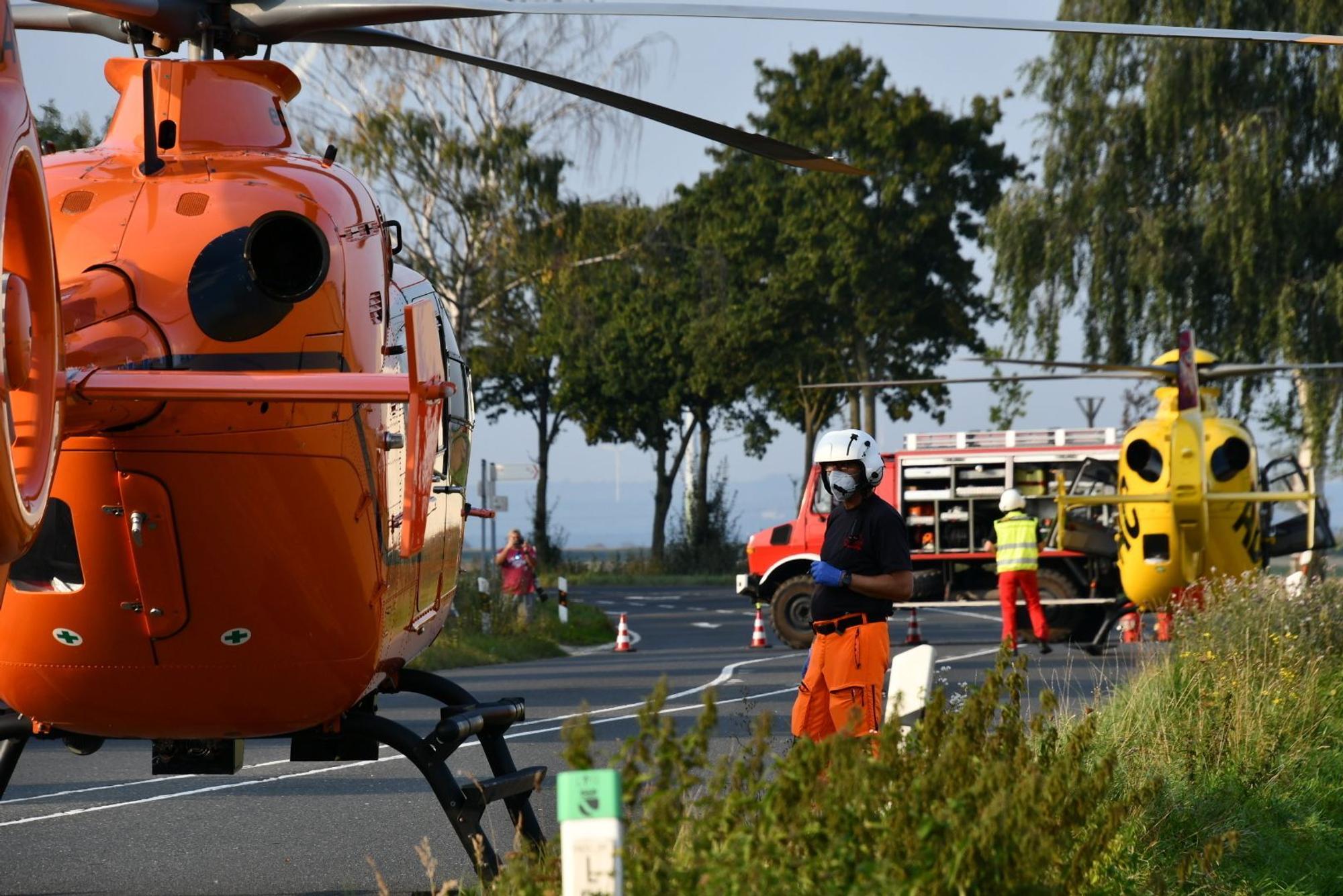Einsatzkräfte stehen neben einem Rettungshubschrauber auf einer Landstraße.