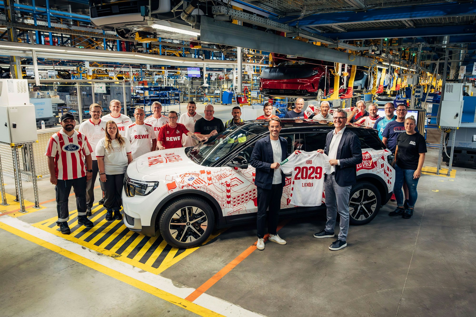 Ford-Mitarbeitende in FC-Trikots und Verantwortliche von FC und Ford posieren rund um ein Ford-Auto.