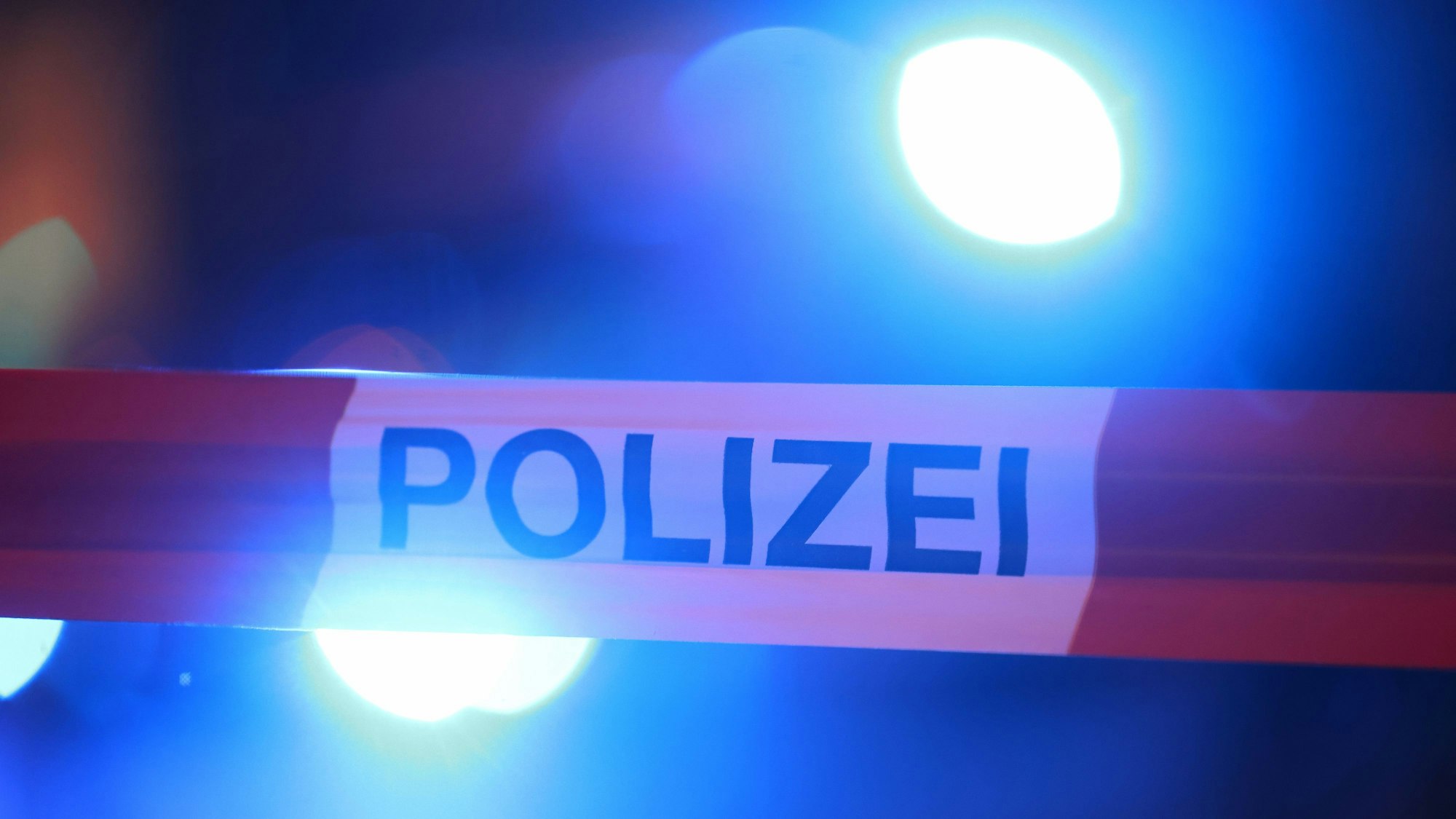 Blaulichter der Polizei leuchten hinter einem Absperrband.