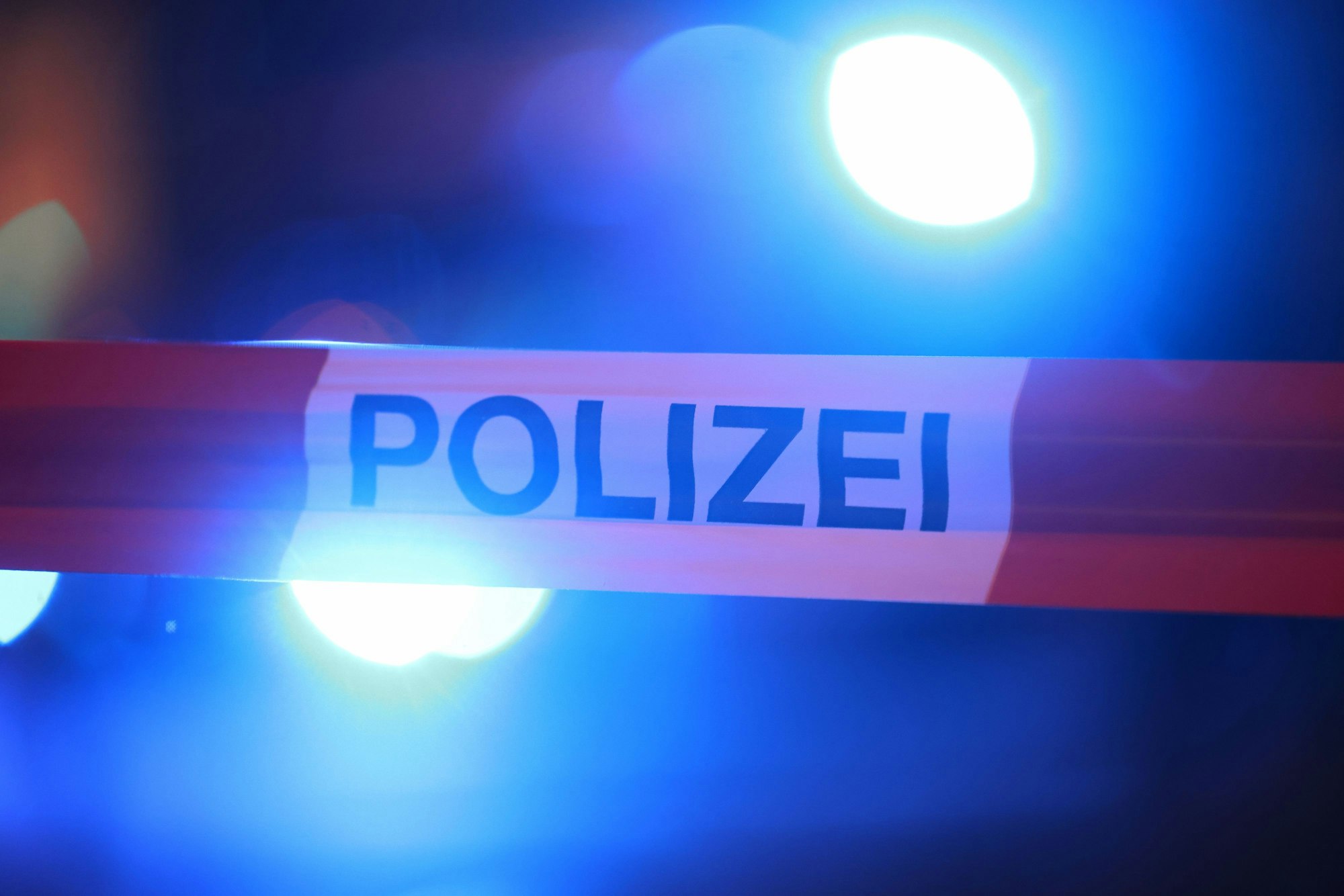 Blaulichter der Polizei leuchten hinter einem Absperrband.