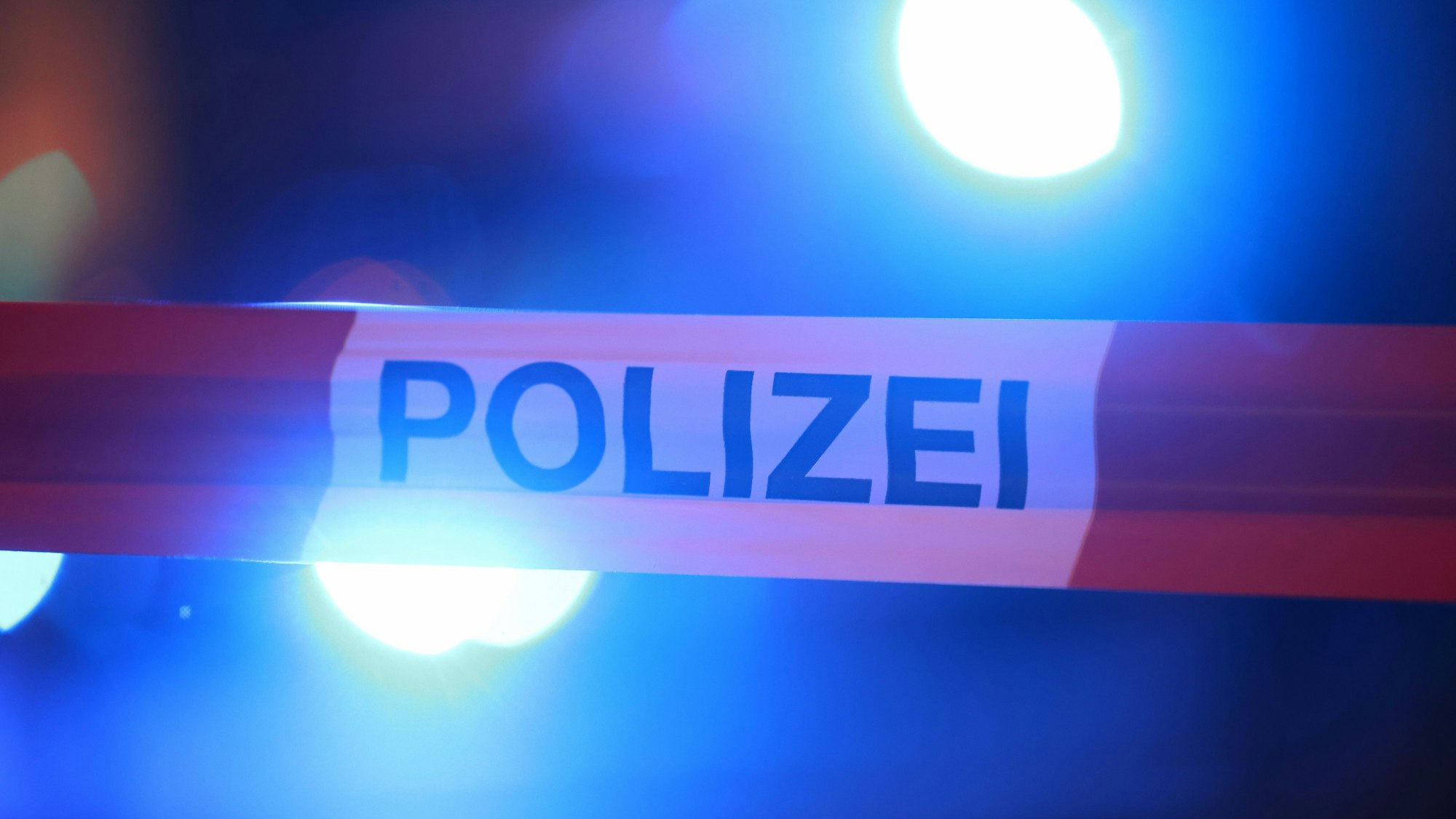 Blaulichter der Polizei leuchten hinter einem Absperrband.