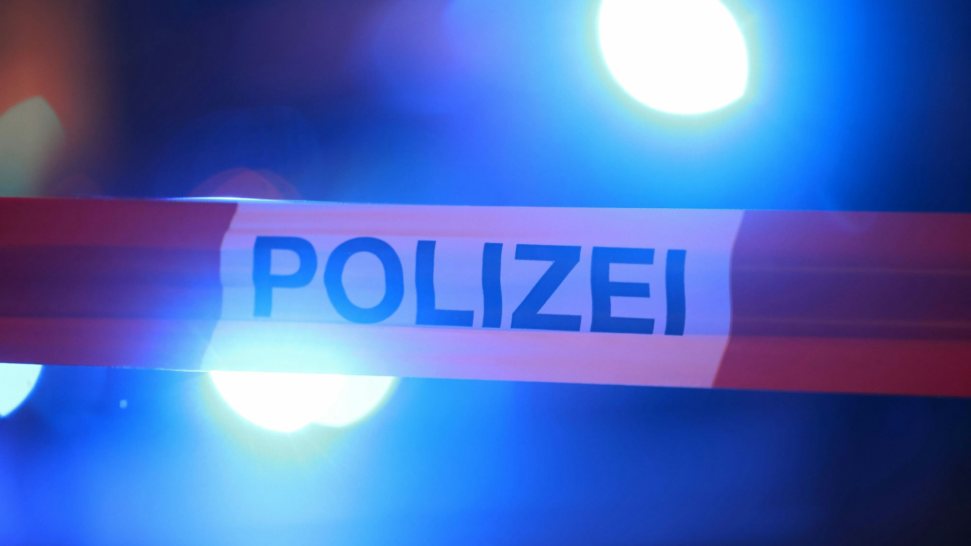 Blaulichter der Polizei leuchten hinter einem Absperrband.