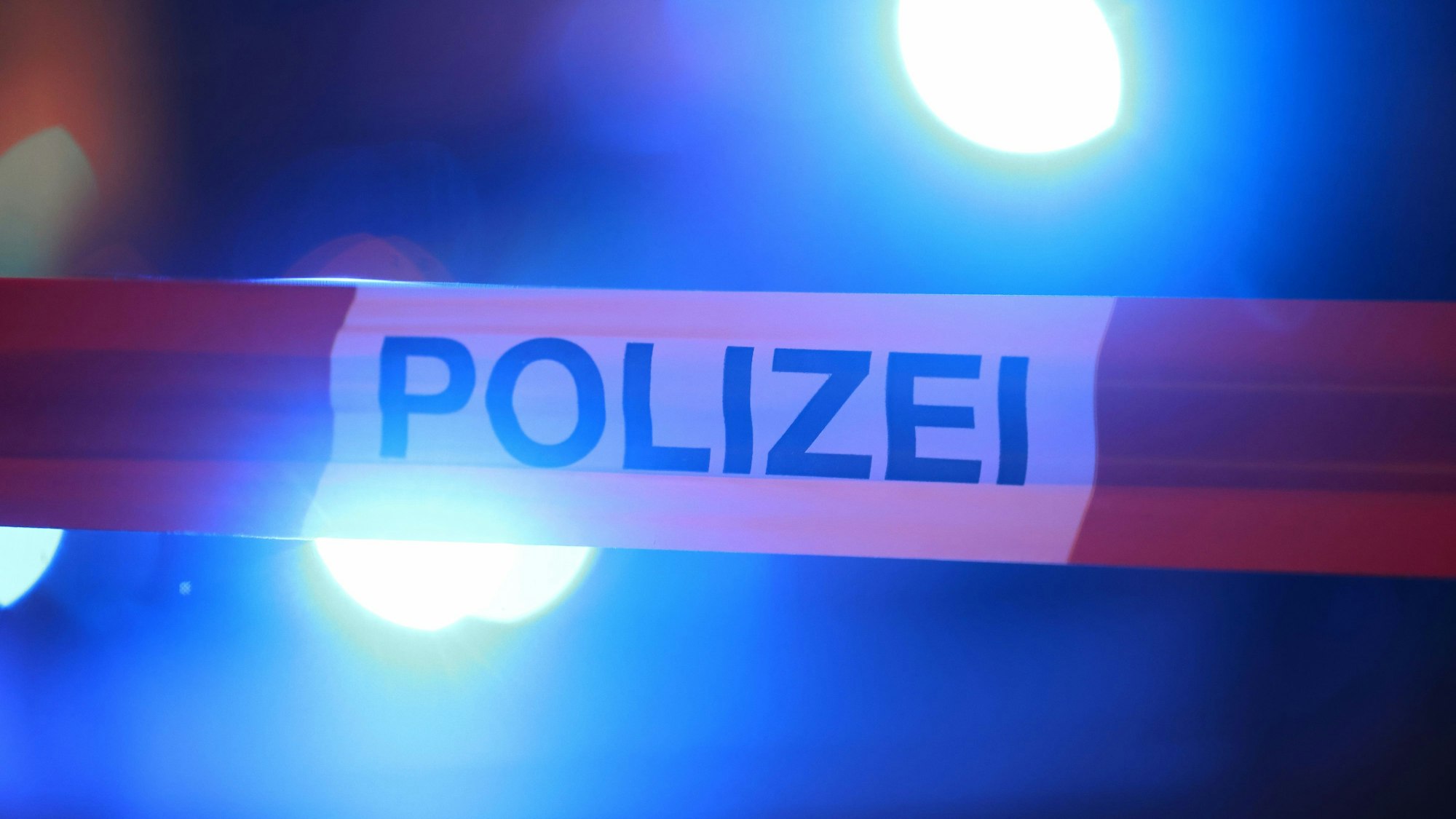 Blaulichter eines Einsatzfahrzeugs der Feuerwehr hinter einem Absperrband.