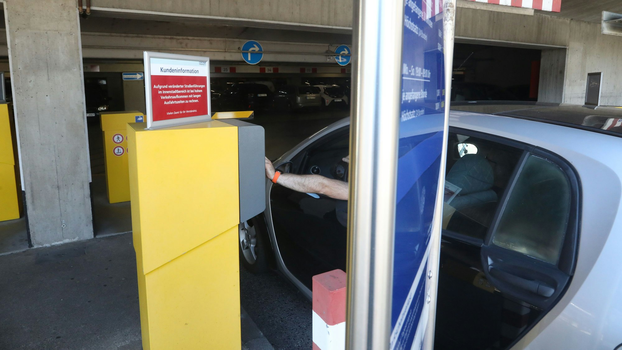 Ein Mann zieht im Auto ein Ticket an der Schranke eines Parkhauses