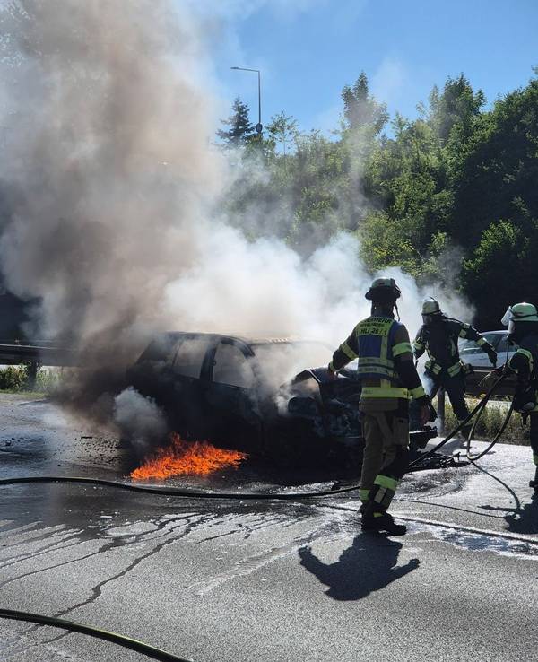 Feuerwehrleute löschen ein brennendes Auto.