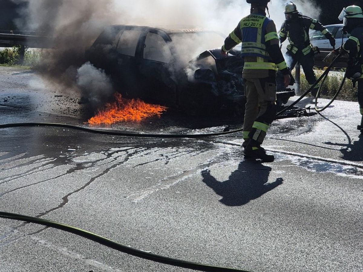 Feuerwehrleute löschen ein brennendes Auto.