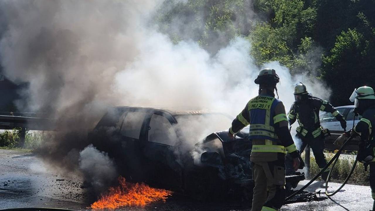 Feuerwehrleute löschen ein brennendes Auto.