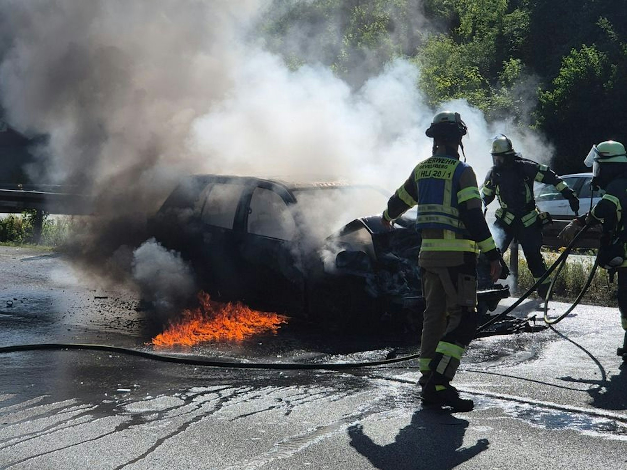 Feuerwehrleute löschen ein brennendes Auto.