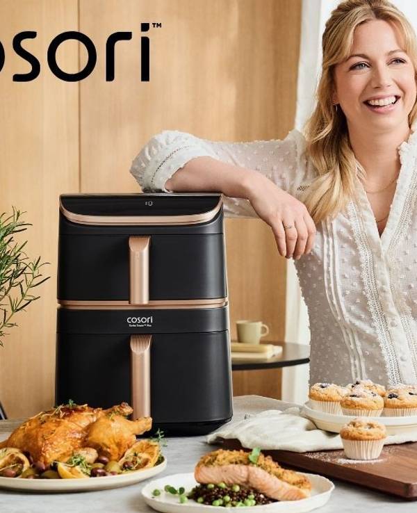 Zora Klipp steht neben dem Cosori Airfryer, umgeben von knusprigen, aber trotzdem gesünder, weil in der Heißluftfritteuse fettärmer zubereiteten Gerichten.