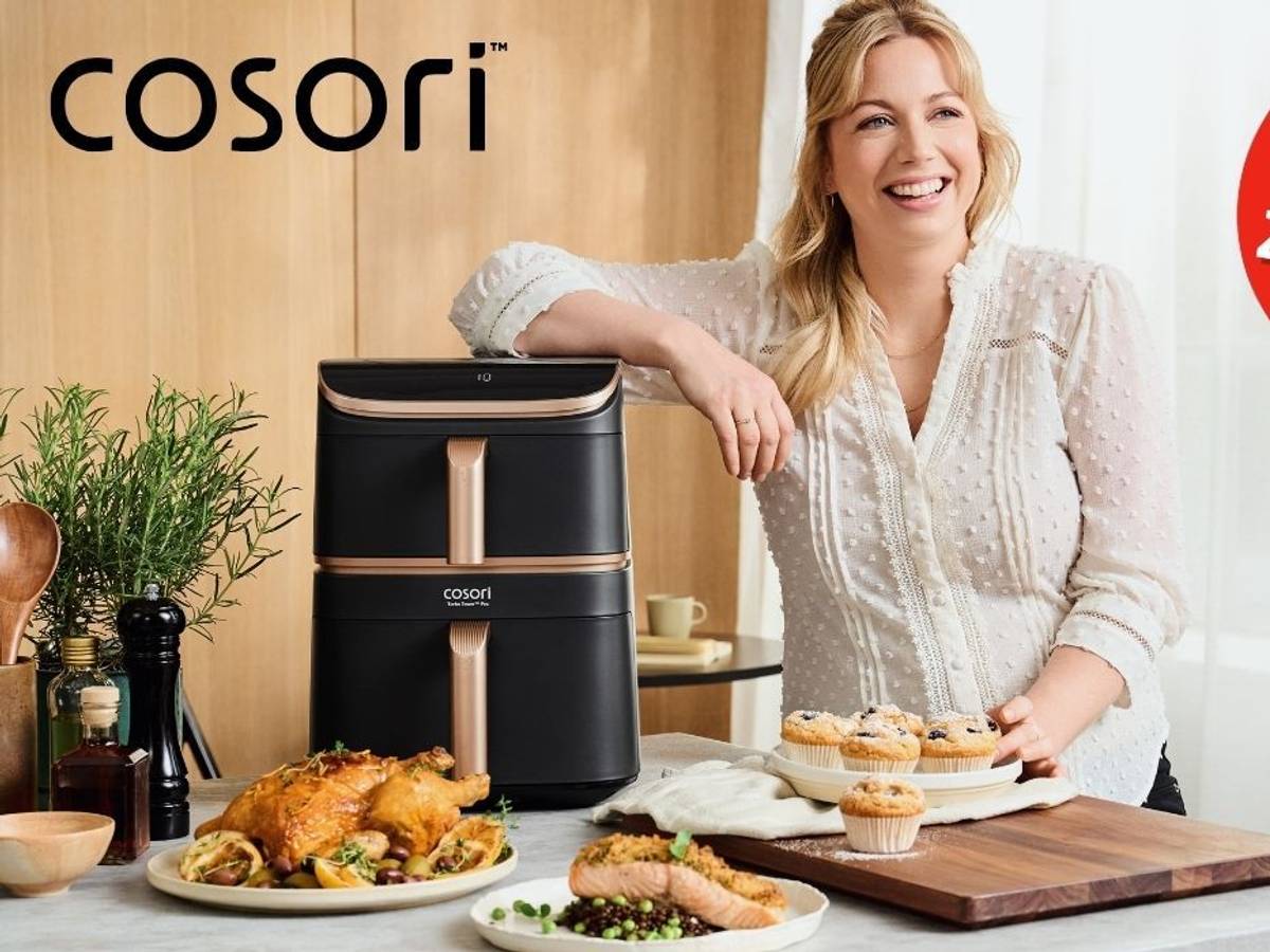Zora Klipp steht neben dem Cosori Airfryer, umgeben von knusprigen, aber trotzdem gesünder, weil in der Heißluftfritteuse fettärmer zubereiteten Gerichten.