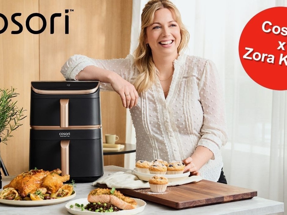 Zora Klipp steht neben dem Cosori Airfryer, umgeben von knusprigen, aber trotzdem gesünder, weil in der Heißluftfritteuse fettärmer zubereiteten Gerichten.