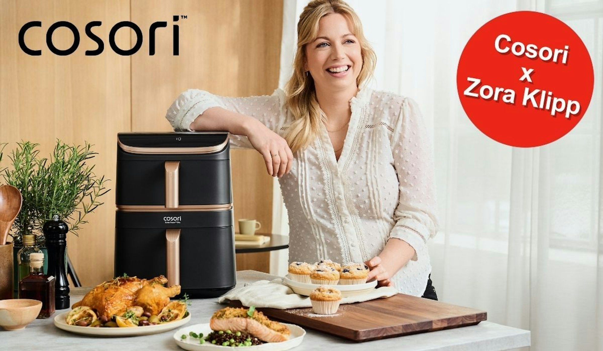 Zora Klipp steht neben dem Cosori Airfryer, umgeben von knusprigen, aber trotzdem gesünder, weil in der Heißluftfritteuse fettärmer zubereiteten Gerichten.