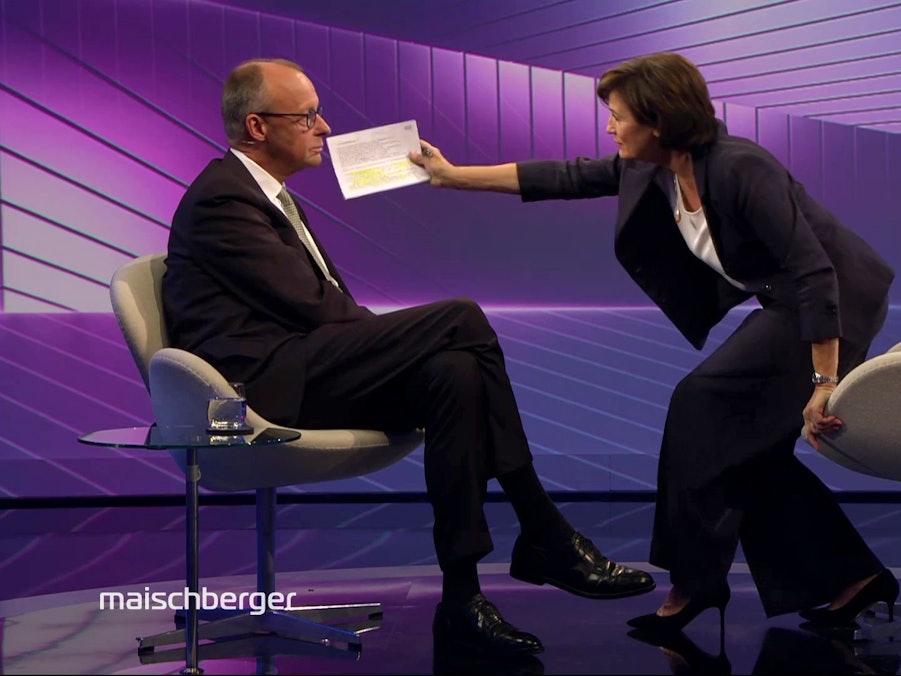Moderatorin Sandra Maischberger wischt Bundeskanzler Friedrich Merz eine Fliege aus dem Gesicht.