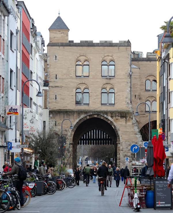Eine Straße, die mit Gebäuden gesäumt ist, führt auf eine historische Burg mit einem Tor zu.