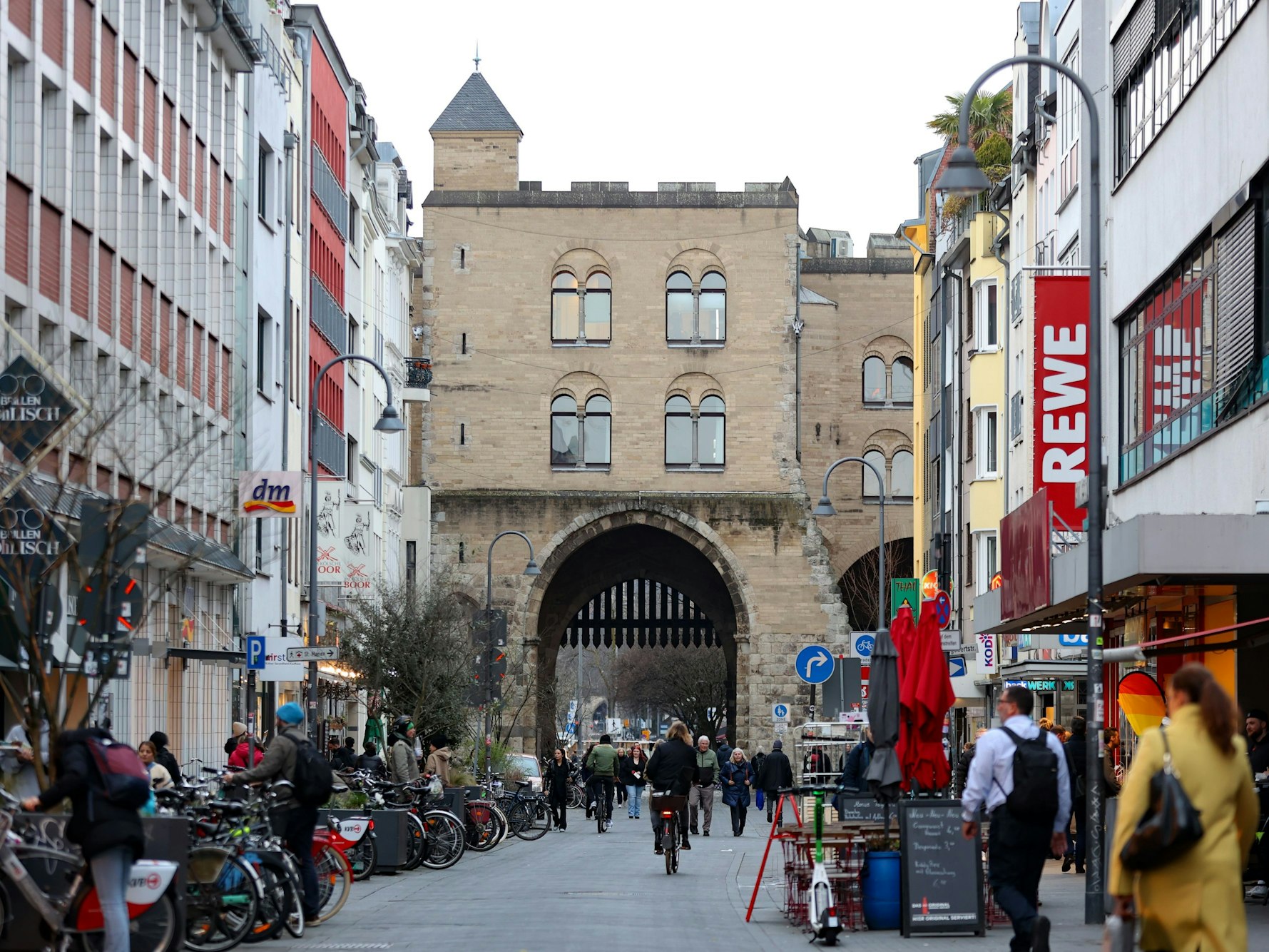 Eine Straße, die mit Gebäuden gesäumt ist, führt auf eine historische Burg mit einem Tor zu.