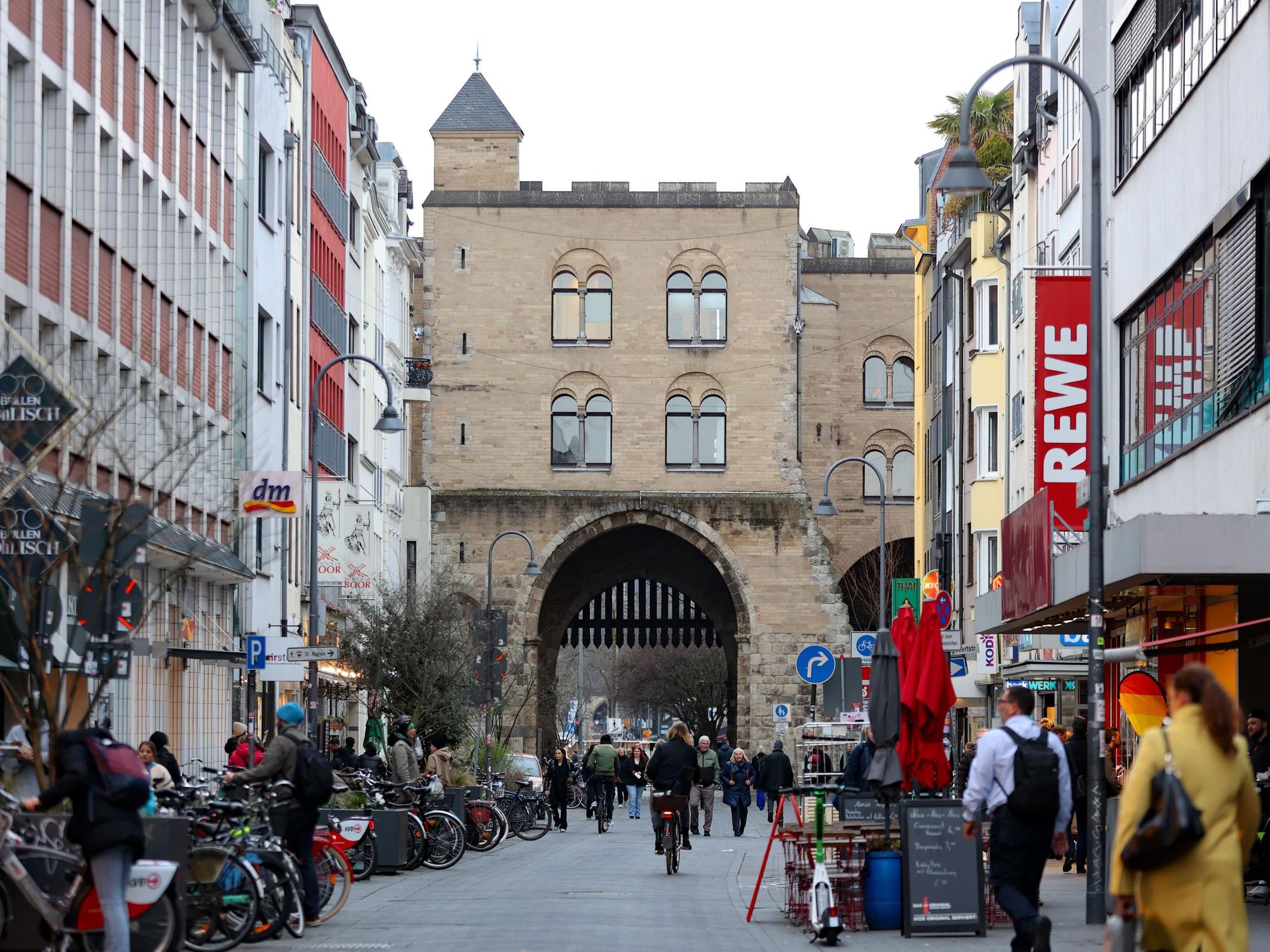 Eine Straße, die mit Gebäuden gesäumt ist, führt auf eine historische Burg mit einem Tor zu.