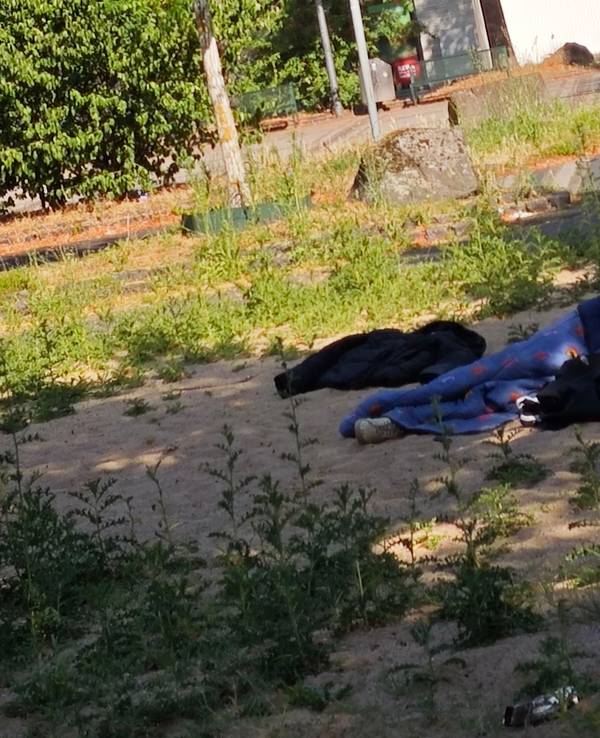 Eine Person liegt auf dem Spielplatz im Sand und schläft.