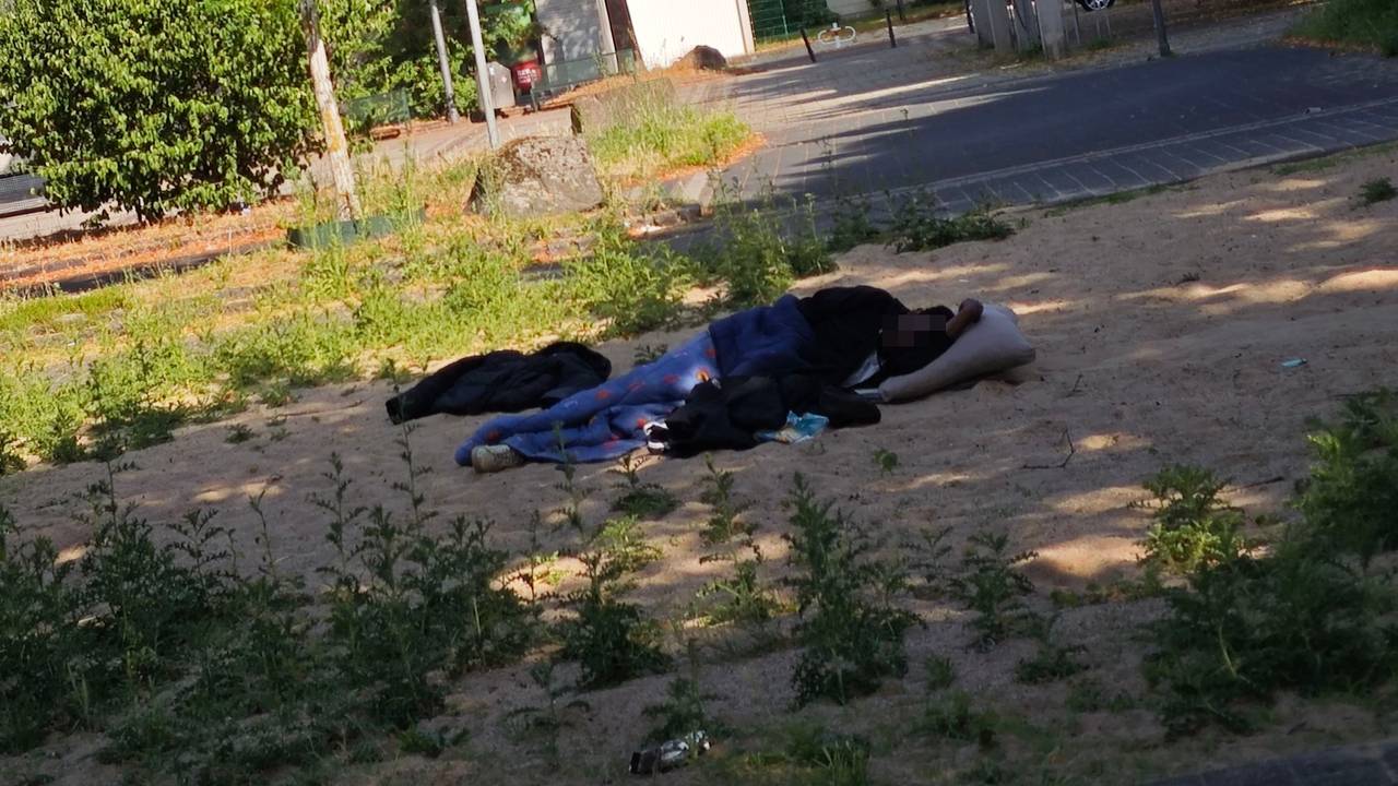 Eine Person liegt auf dem Spielplatz im Sand und schläft.