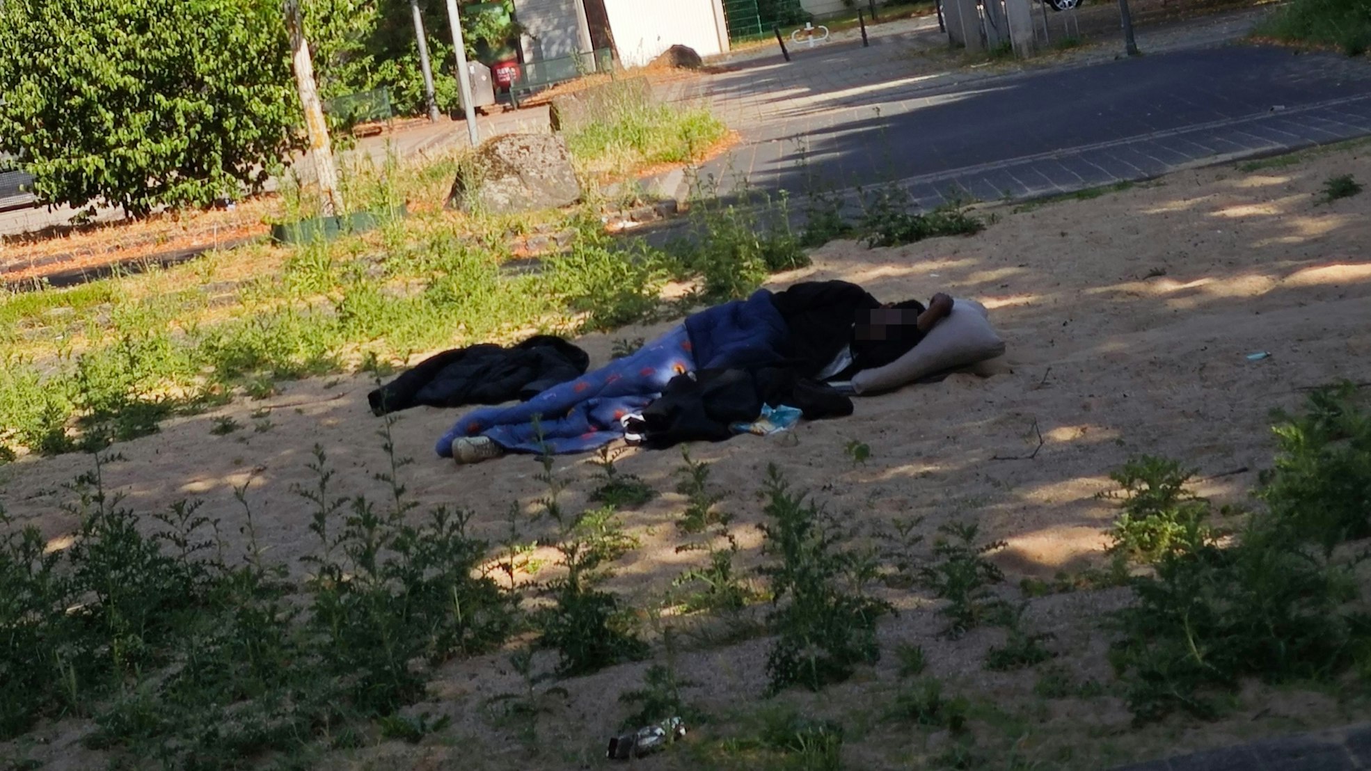 Eine Person liegt auf dem Spielplatz im Sand und schläft.