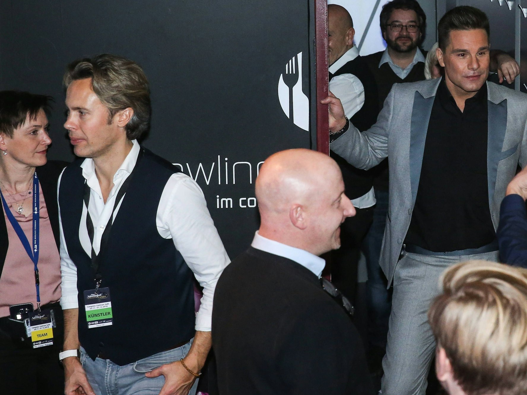 Menschen laufen durch einen Backstagebereich mit schwarzer Wandverkleidung