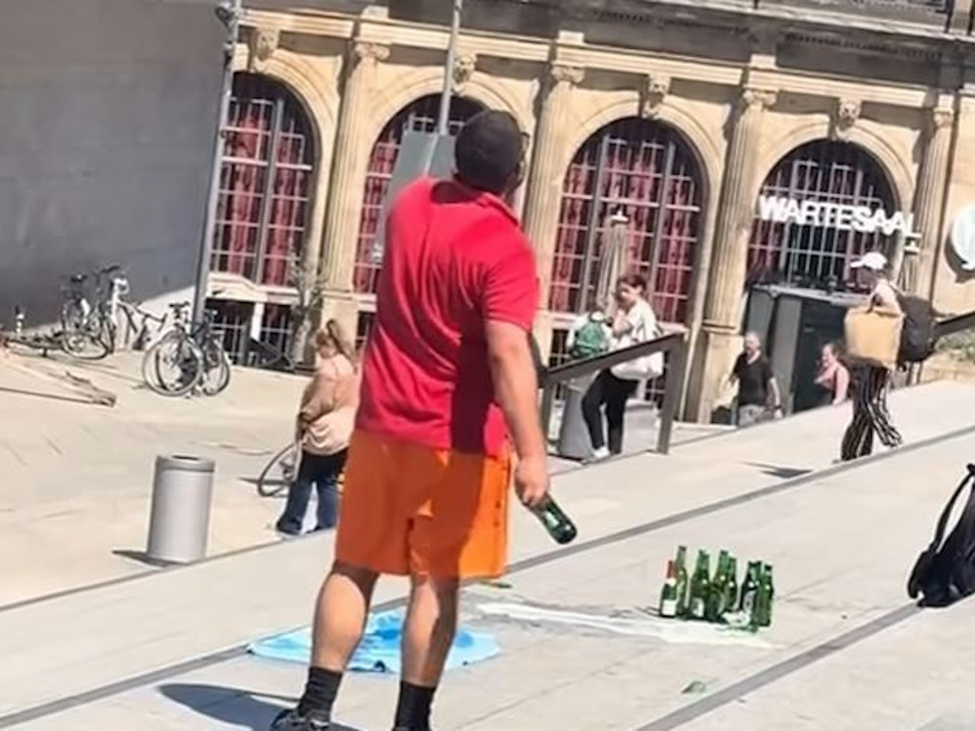 Hier wirft der unbekannte Mann eine Bierflasche von der Domtreppe am Kölner Hauptbahnhof.