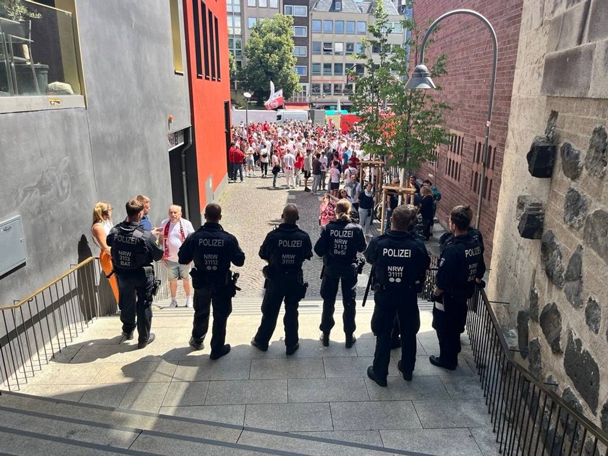Im Vordergrund stehen Polizisten auf einer Treppe, im Hintergrund sind FC-Fans zu sehen.