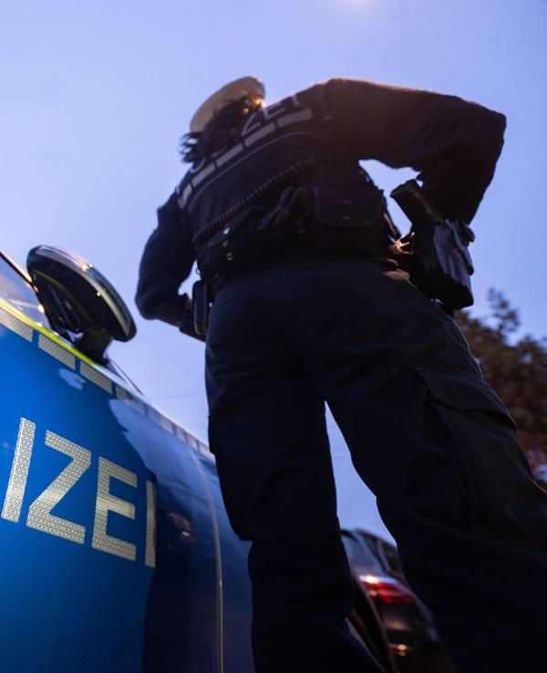 Ein Polizist steht neben einem Streifenwagen.