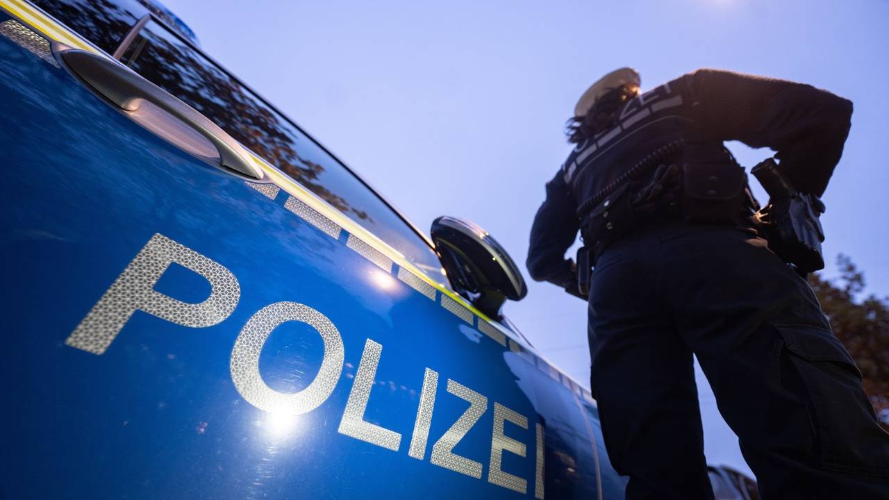 Ein Polizist steht neben einem Streifenwagen.