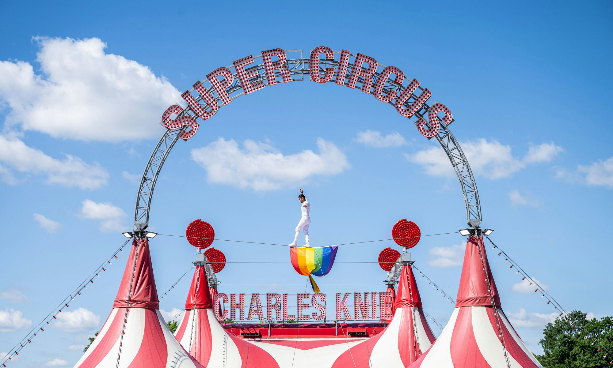 Der Hochseilartist David Ruiz vom Zirkus Charles Knie balanciert auf einem Seil über dem Zirkuszelt, wo eine Regenbogenfahne aus Protest hängt.