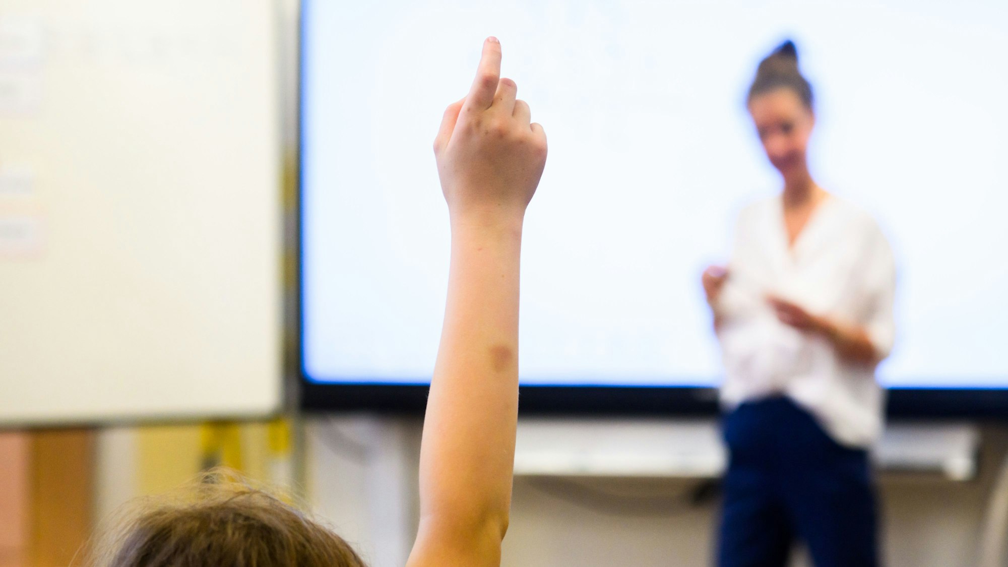Eine Schülerin meldet sich, während die Lehrerin vor der Klasse steht.