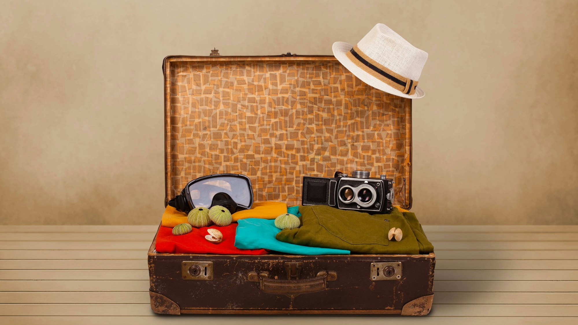 Ein aufgeklappter Koffer mit Taucherbrille, Hut und Handtüchern