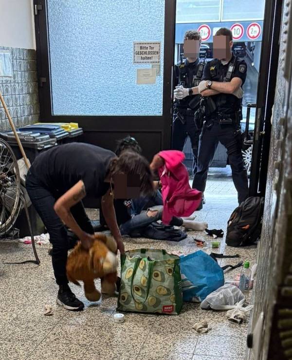 Zwei Drogenabhängige im Hausflur in der Lungengasse. Zwei Polizisten stehen mit verschränkten Armen in der Tür.