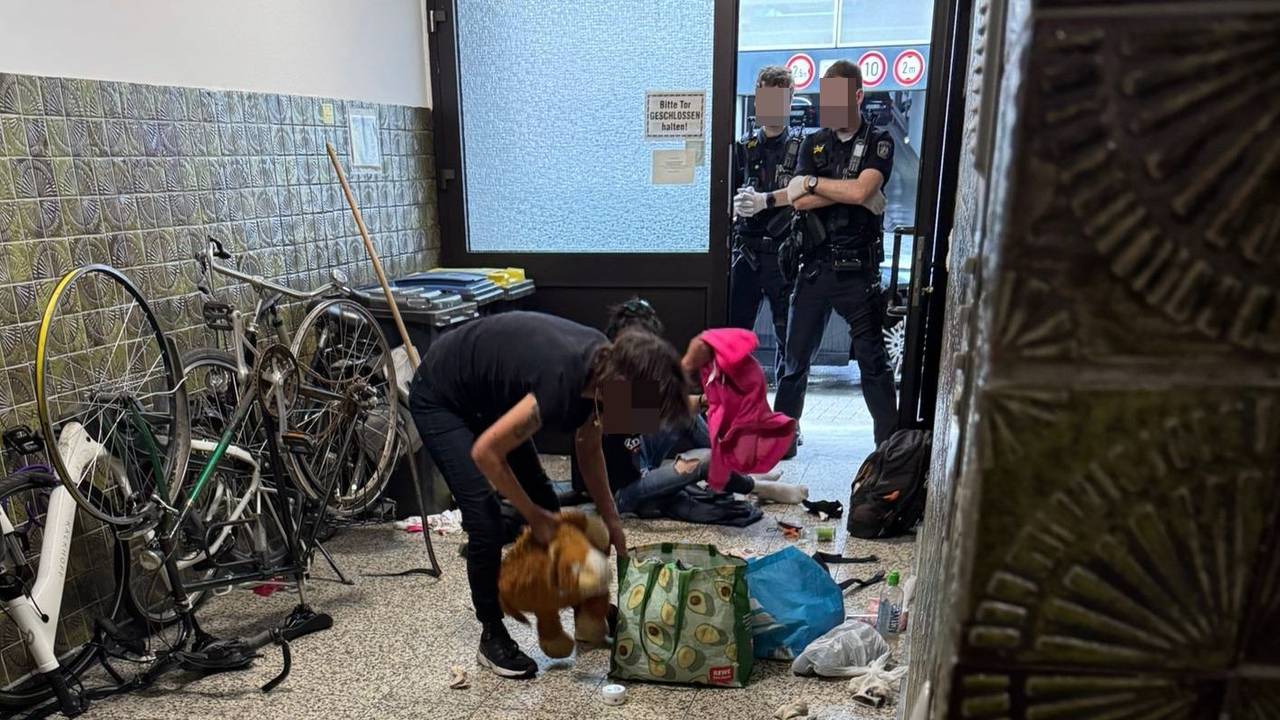 Zwei Drogenabhängige im Hausflur in der Lungengasse. Zwei Polizisten stehen mit verschränkten Armen in der Tür.