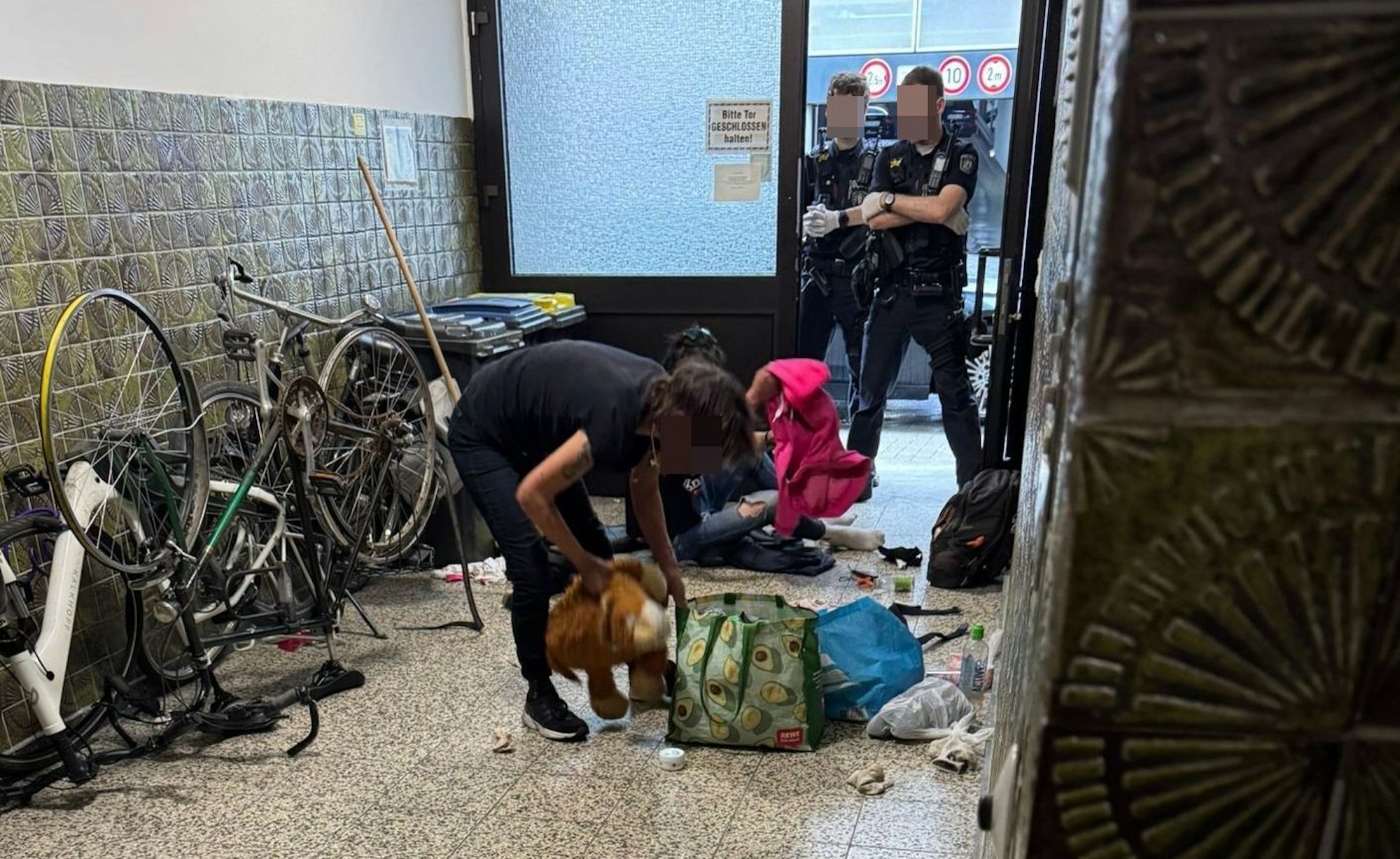 Zwei Drogenabhängige im Hausflur in der Lungengasse. Zwei Polizisten stehen mit verschränkten Armen in der Tür.