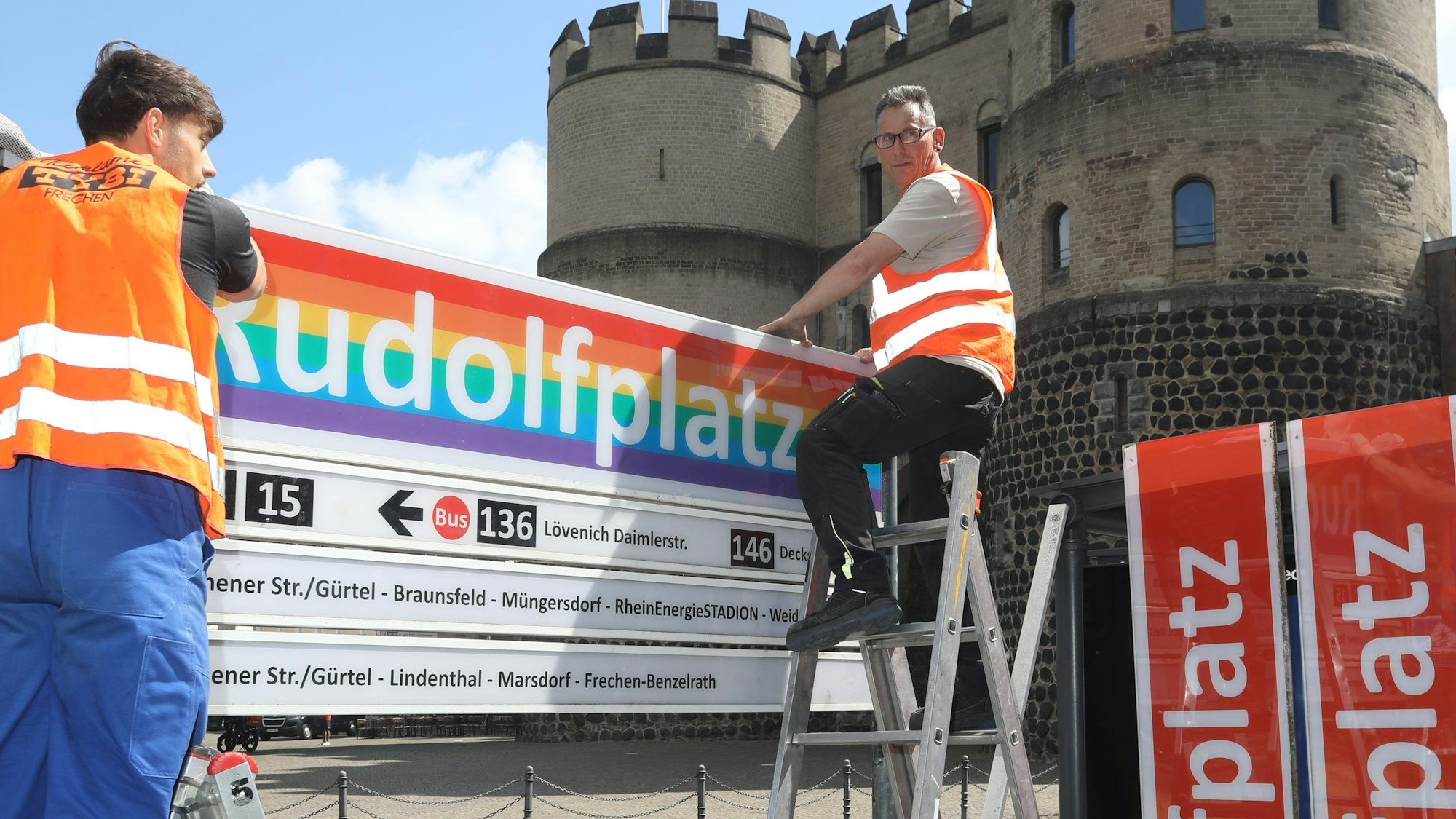Ein regenbogenfarbenes KVB-Schild an der Haltestelle Rudolfplatz in Köln.