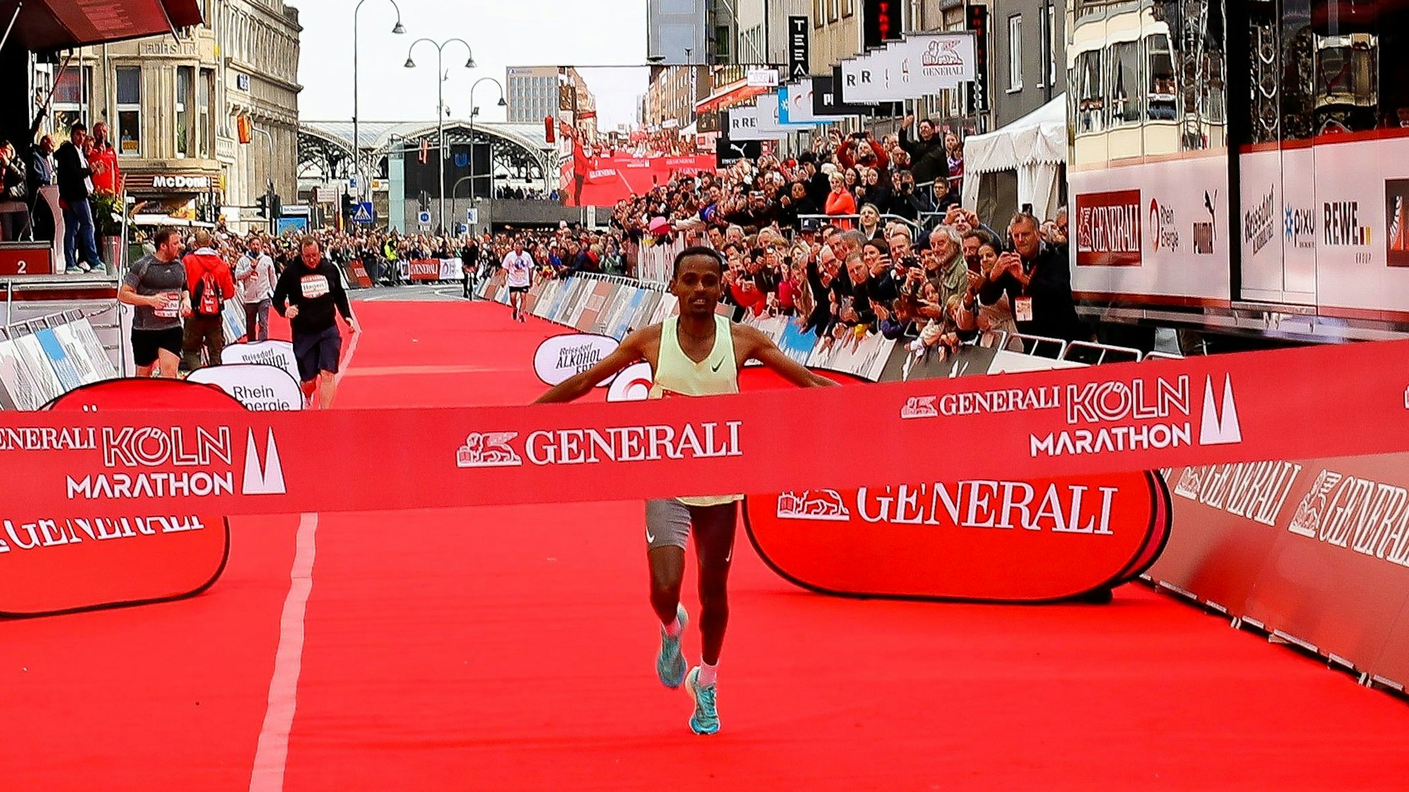 Temeke Tadesse aus Äthiopien läuft durch das Zielband, auf dem „Generali Köln Marathon“ steht. Am Rand stehen zahlreiche Menschen.