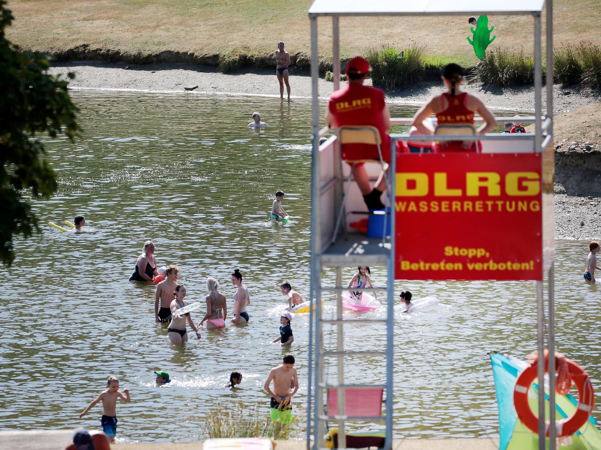 Menschen planschen in einem Badesee, beobachtet von DLRG-Rettungsschwimmern