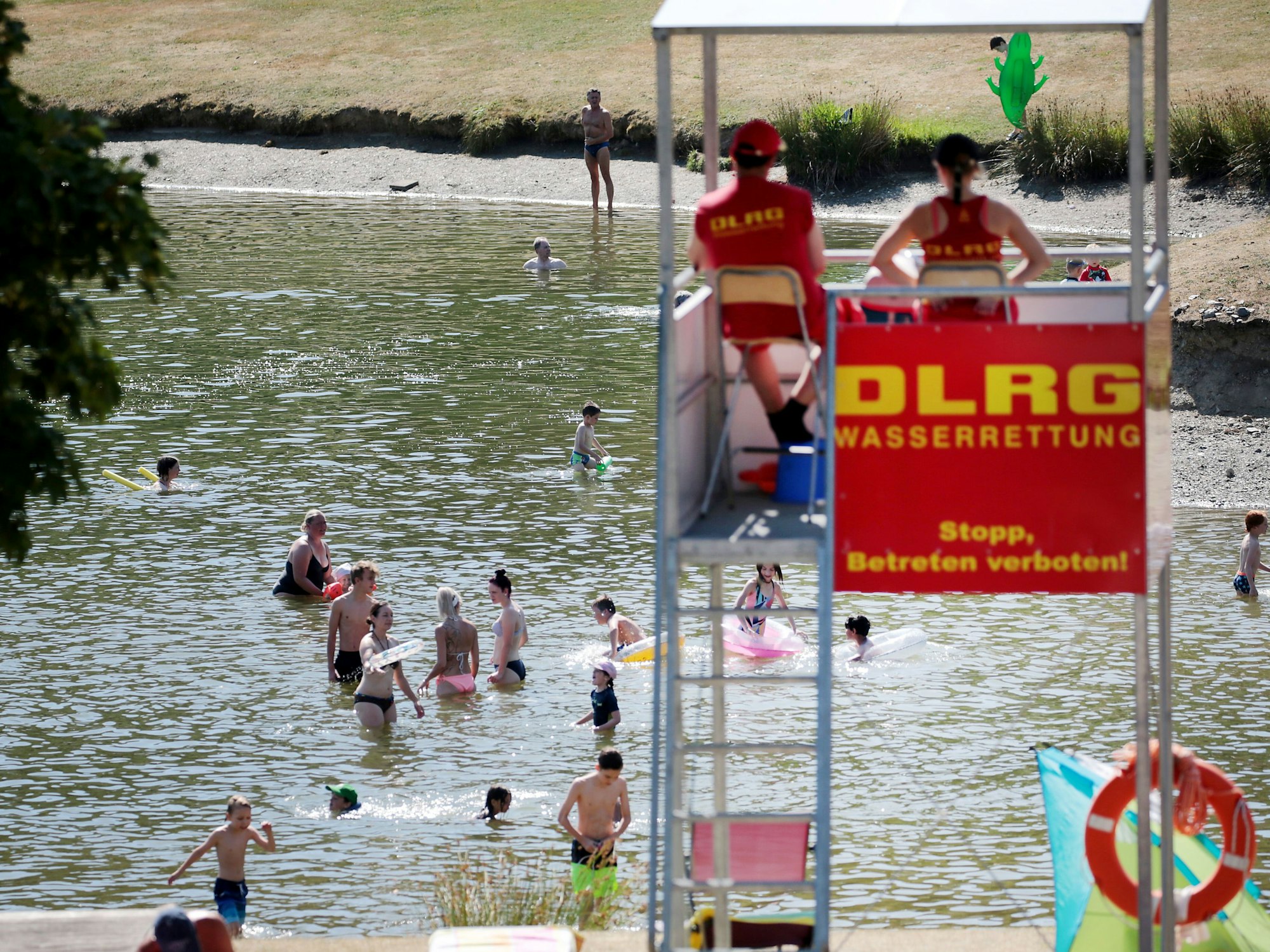 Menschen planschen in einem Badesee, beobachtet von DLRG-Rettungsschwimmern