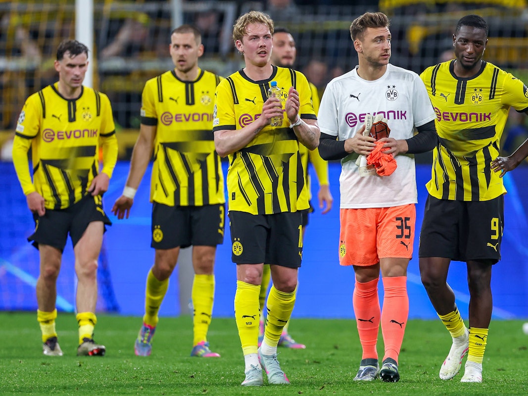 Marcel Lotka geht zwischen Julian Brandt und Serhou Guirassy über den Rasen im Signal-Iduna-Park.