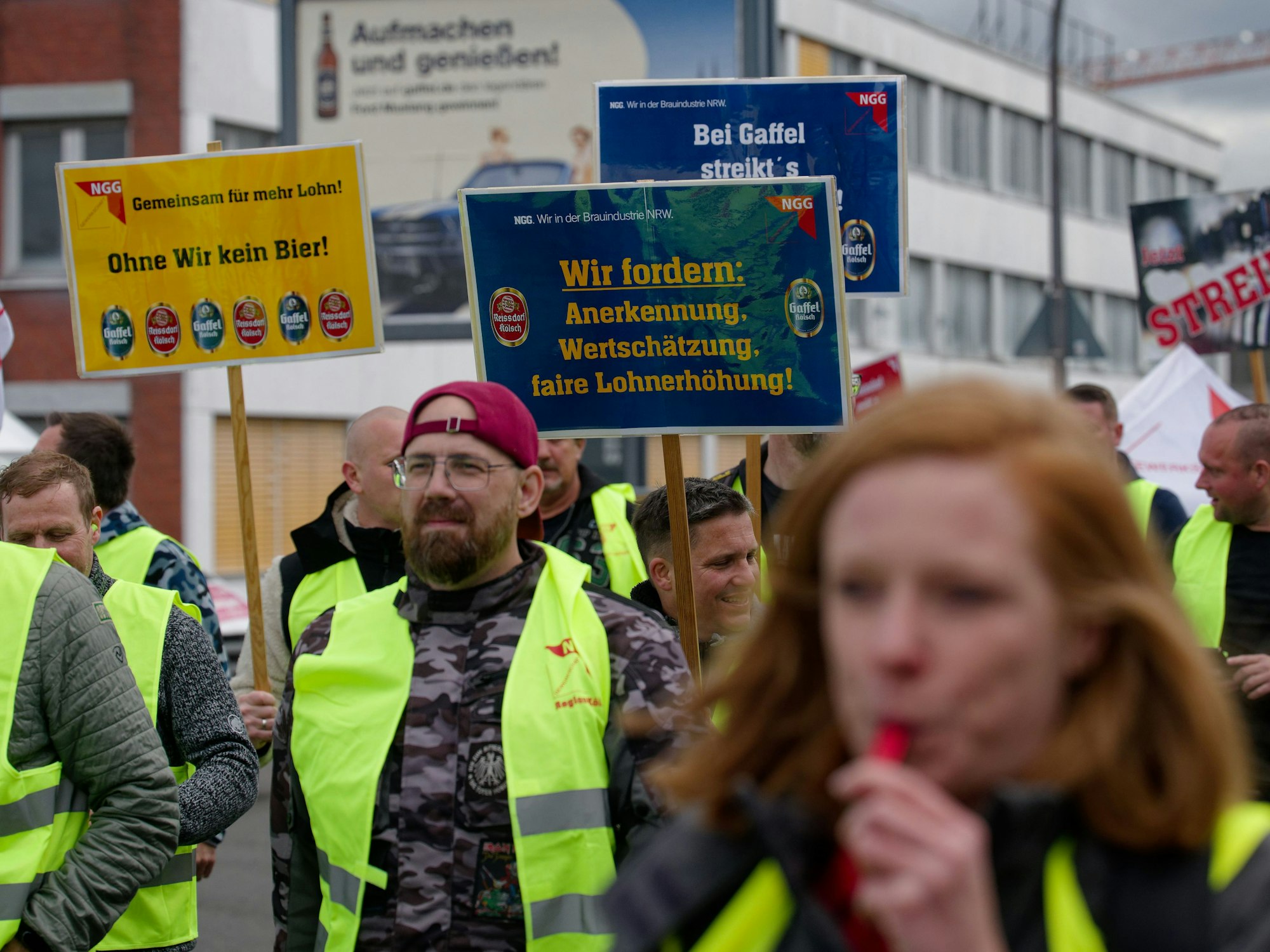 Mitarbeiter der beiden Kölsch-Brauereien Gaffel und Reissdorf halten bei einem Warnstreik im Mai 2025 vor der Gaffelbrauerei in Köln-Porz Schilder.