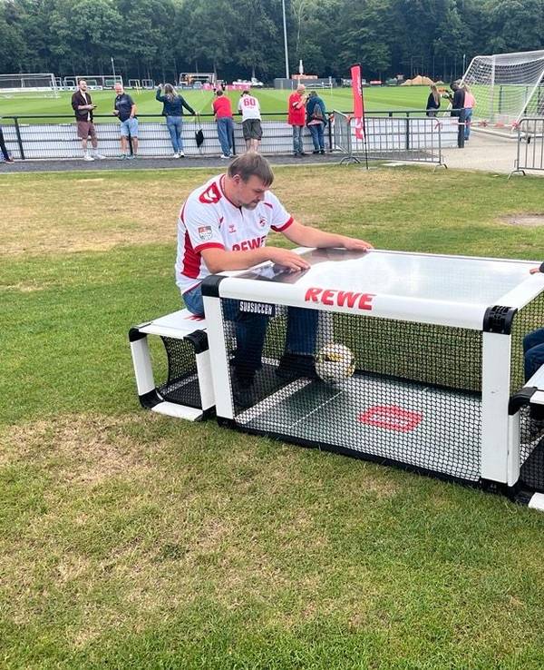 Ein Mann und ein Junge sitzen an einem Sitzfußball-Modul.