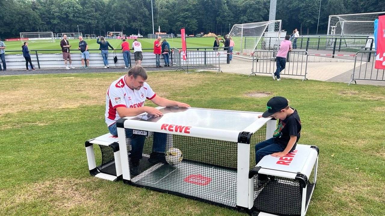 Ein Mann und ein Junge sitzen an einem Sitzfußball-Modul.