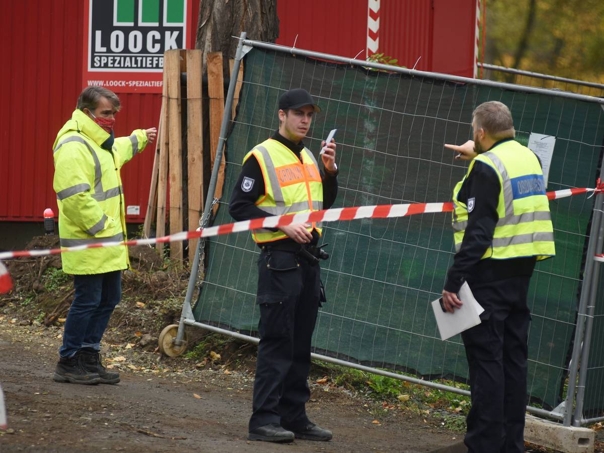 Drei Männer stehen an einer Polizeiabsperrung.