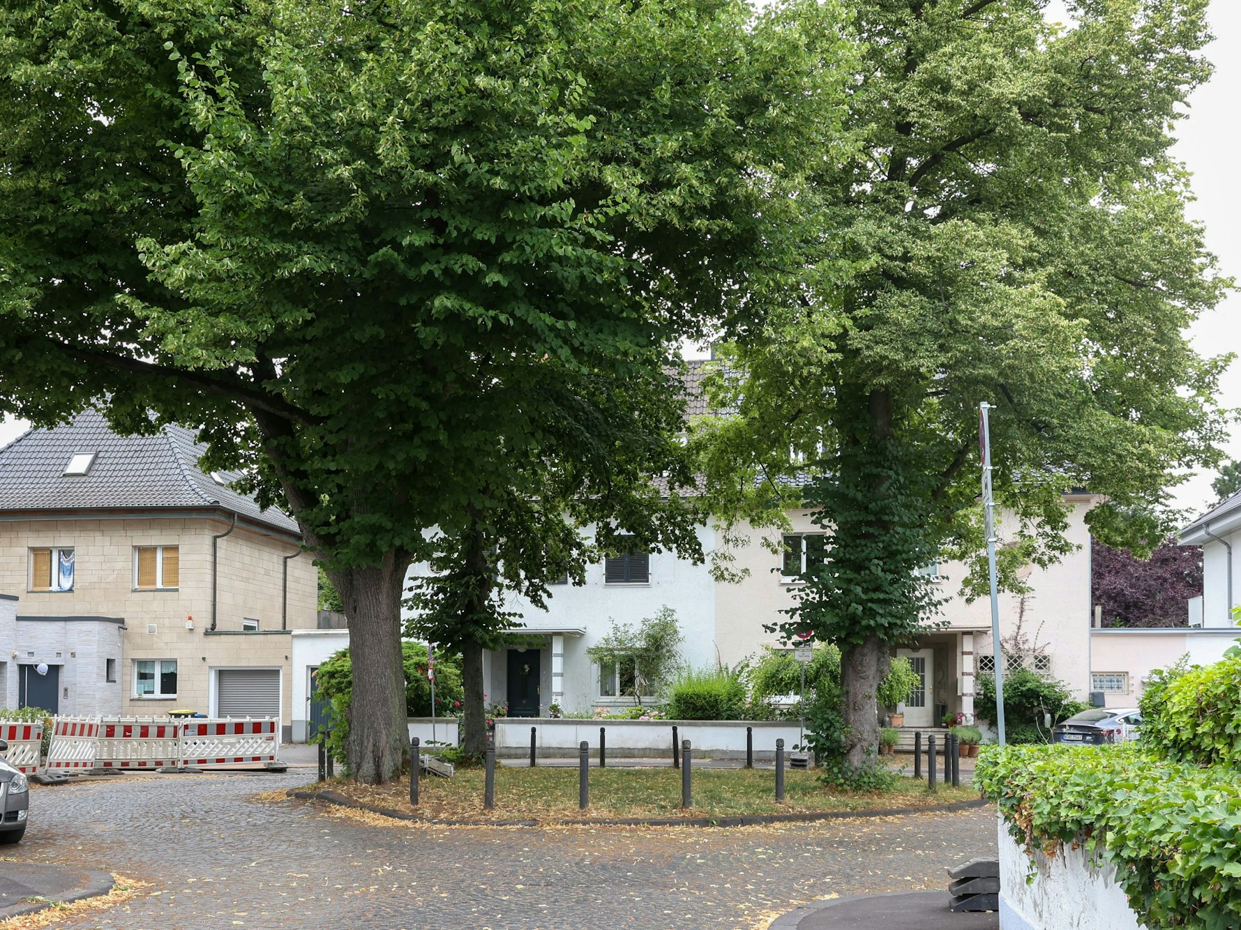 Häuser stehen um ein Rondell mit Bäumen, eine Straße, die davon abzweigt, ist abgesperrt.