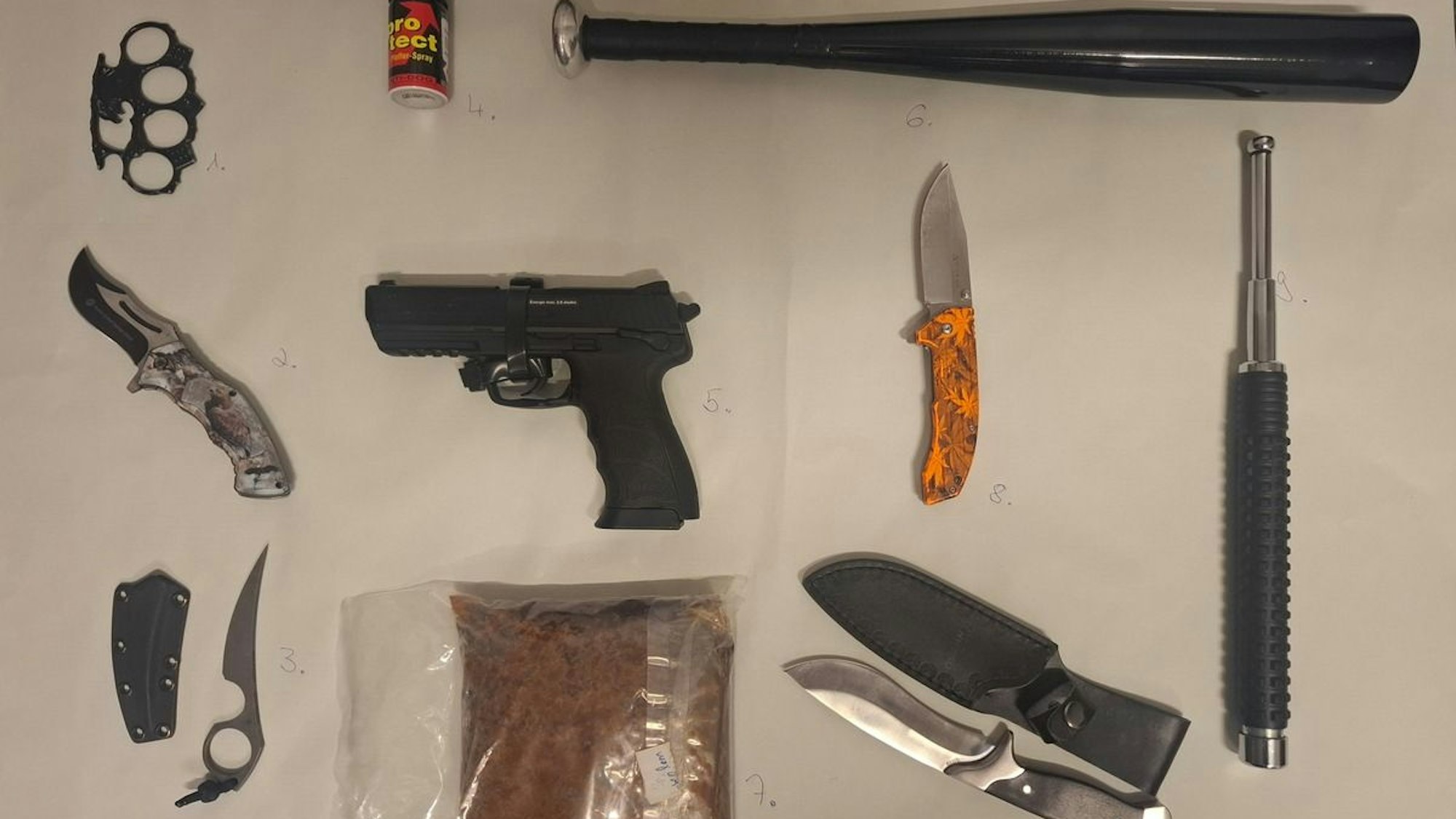 Sichergestellte Waffen und Gegenstände wie Messer, Schlagring und Baseballschläger liegen auf einem Tisch.