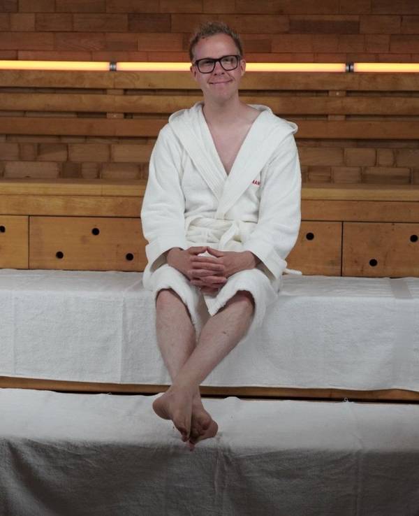 Ein Mann im weißen Bademantel sitzt auf der Holzstufe einer Sauna